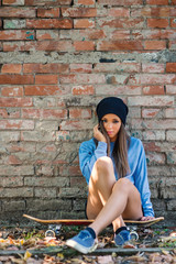 Teenager intimate portrait sit on skateboard against brick wall.