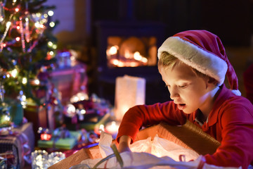 Lovely little boy with a santa claus hat opens a gift in front o