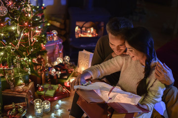 Handsome couple opening a gift in front of the Christmas tree li