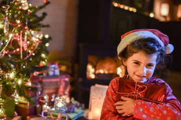 Lovely little girl opens a gift in front of the Christmas tree l