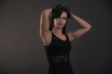 Fototapeta premium Cute brunette teenage girl with hands in hair wearing black dres