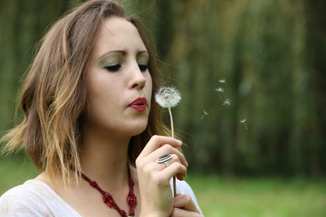 Beautiful young woman blowing a dandelion