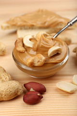 Fototapeta na wymiar Creamy peanut butter in bowl and bread slices on wooden table