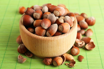 Hazelnuts in wooden bowl on bamboo mat background