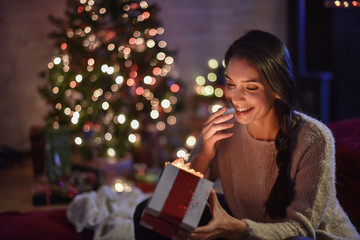 beautiful young woman opening her gift on Christmas Eve with a C
