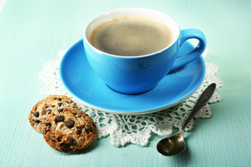 Glass cup of coffee and tasty cookie on color wooden background