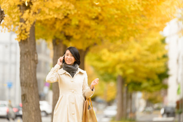 電話しながらイチョウ並木を歩く女性