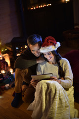 Romantic couple sharing a digital tablet near a wood stove on a