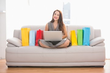 Smiling brunette shopping online with laptop on the couch