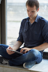 businessman sitting on window sill with the tablet