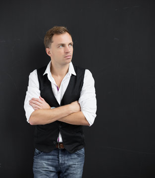Young man standing with arms crossed against dark wall
