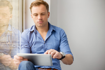 Young creative man sitting at window and using ipad