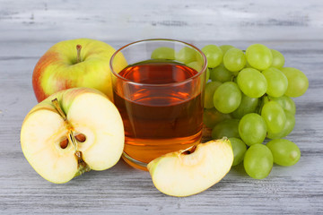 glass of juice with fresh grape and apples on grey wooden table