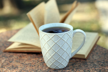 Fototapeta na wymiar Cup with hot drink and book, outdoors