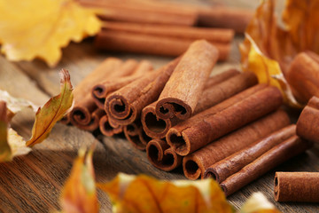 Cinnamon sticks with yellow leaves on wooden background