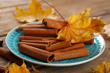 Cinnamon sticks on plate with yellow leaves on wooden