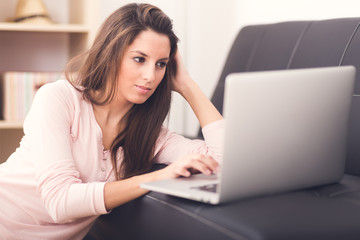 Smiling young woman looking on your laptop sitting on floor at h