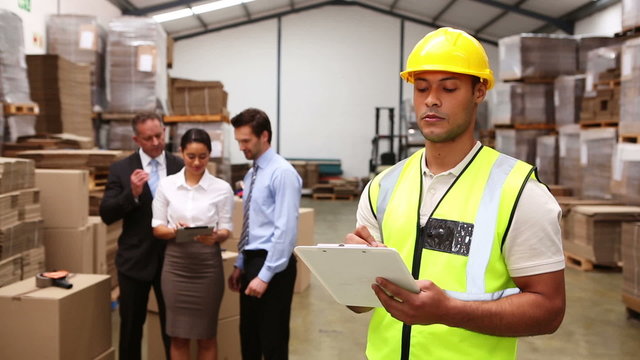 Warehouse managers talking while worker uses tablet pc