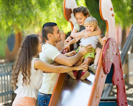 Smiling Parents Helping Kids On Slide