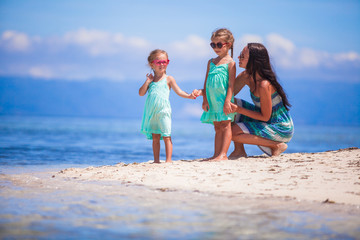 Fototapeta na wymiar Adorable little girls and young mother on tropical white beach