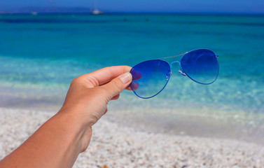 Close up of colorful blue sunglasses in hand on tropical beach