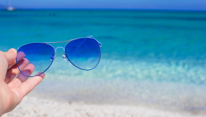 Close up of colorful blue sunglasses in hand on tropical beach