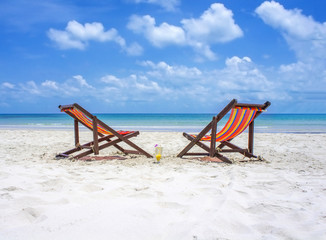 Two beach chairs on the white sand beach before blue sea