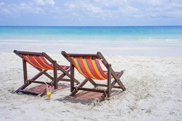 Two beach chairs on the white sand beach before blue sea