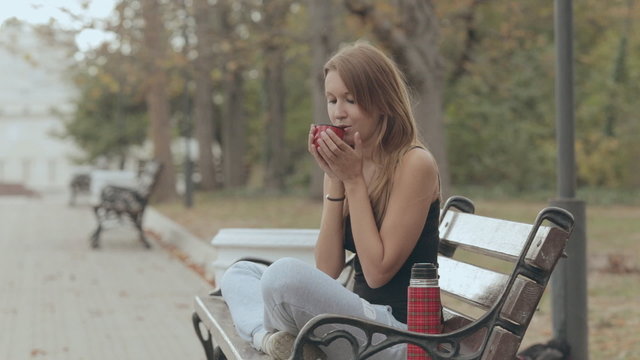 Cute girl blowing on hot tea from a thermos and drink it