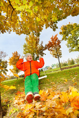 Boy sitting on swings, smiling during autumn day