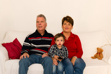 Grandchild and grandparents watching tv on a white sofa
