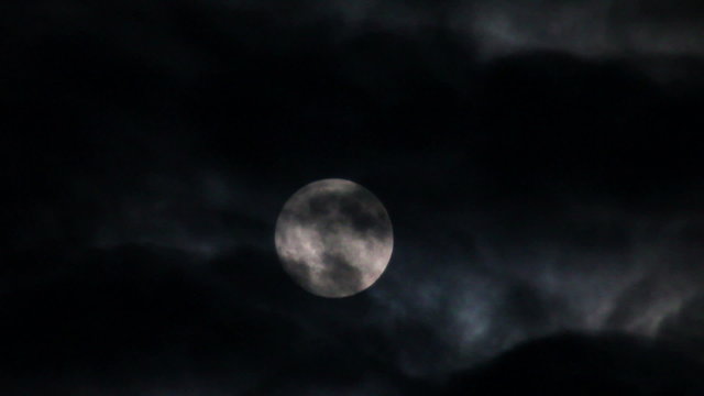 full moon moving between clouds