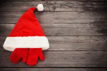 Santa's hat and red mitten on old wooden background