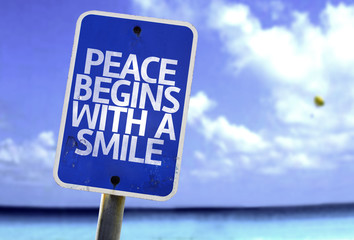 Peace Begins With a Smile sign with a beach on background