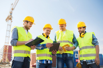 group of smiling builders with tablet pc outdoors