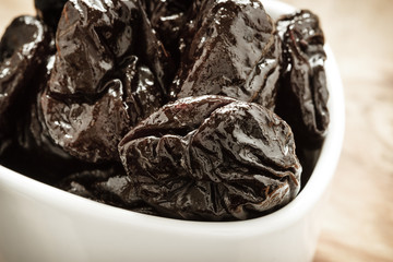 dried plums prunes in white bowl on wooden table