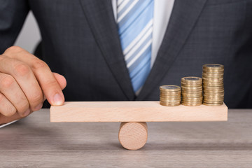 Businessman Balancing Coins On Wooden Seesaw