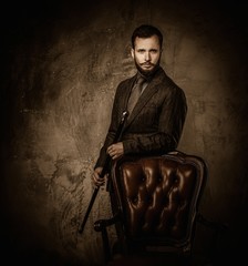 Handsome well-dressed man with stick standing near leather chair