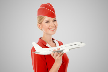 Charming Stewardess Holding Airplane In Hand. Gray Background.