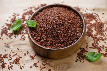 Raw red kernel rice in a wooden bowl with basil, horizontal shot