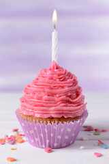 Delicious birthday cupcake on table on light purple background