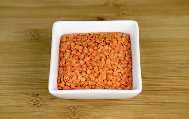 Macro of red split lentils in white bowl on wooden board
