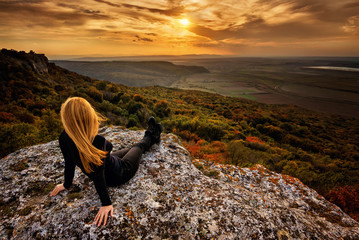 A woman enjoys the view of sunset over an autumn forest