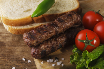 Kebapche with vegetables and bread on wooden board