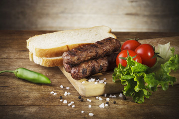 Kebapche with vegetables and bread on wooden board