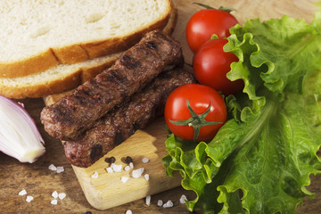 Kebapche with vegetables and bread on wooden board