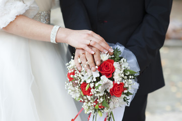 Hands of bride and groom with rings on wedding bouquet of roses