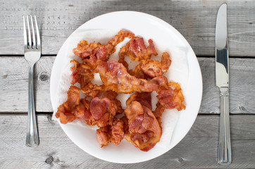 Fried bacon on a ceramic plate against wooden background 