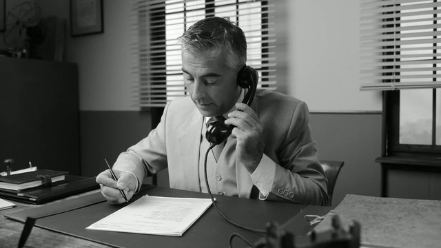 Smiling businessman working at office desk and having a phone ca