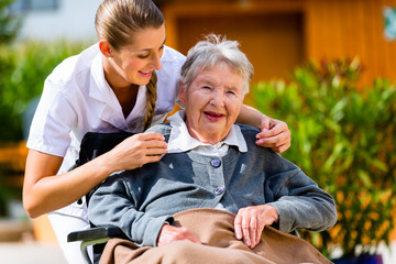 Pflegerin hält Hand alter Frau im Rollstuhl